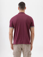 A man wearing a short-sleeve polo shirt in maroon with gray sleeve trim and a half-zip collar, paired with beige cargo pants, against a plain white studio background.