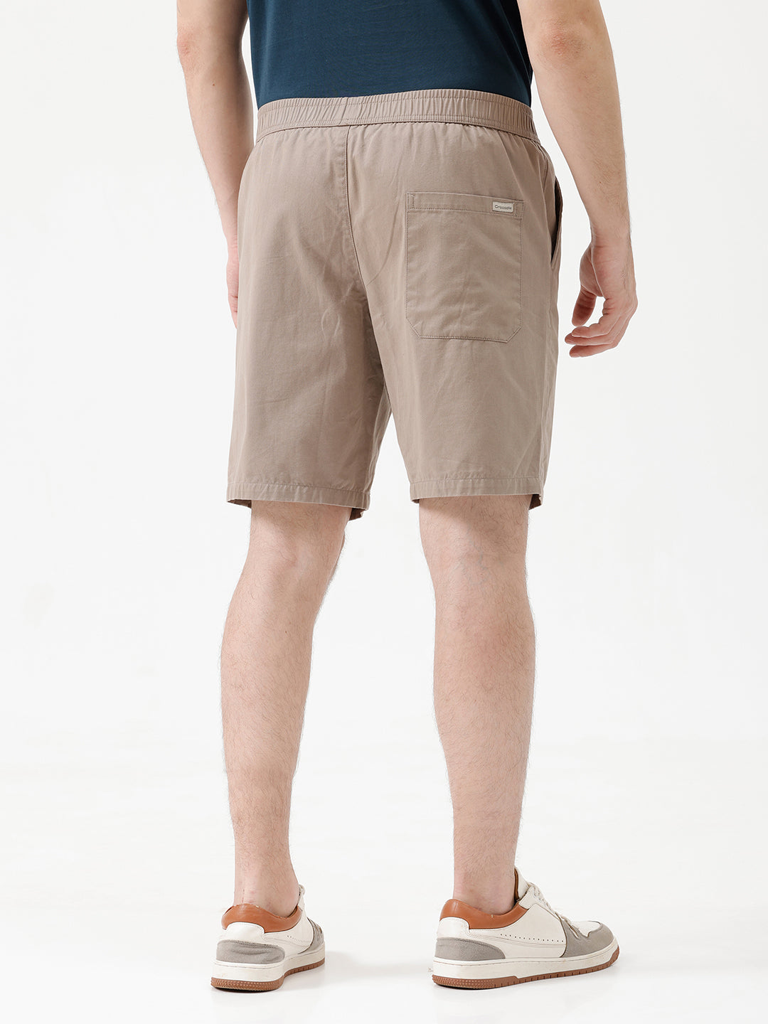 A person wearing beige drawstring shorts, a navy blue t-shirt, and white sneakers, shown from the waist down against a plain white studio background.