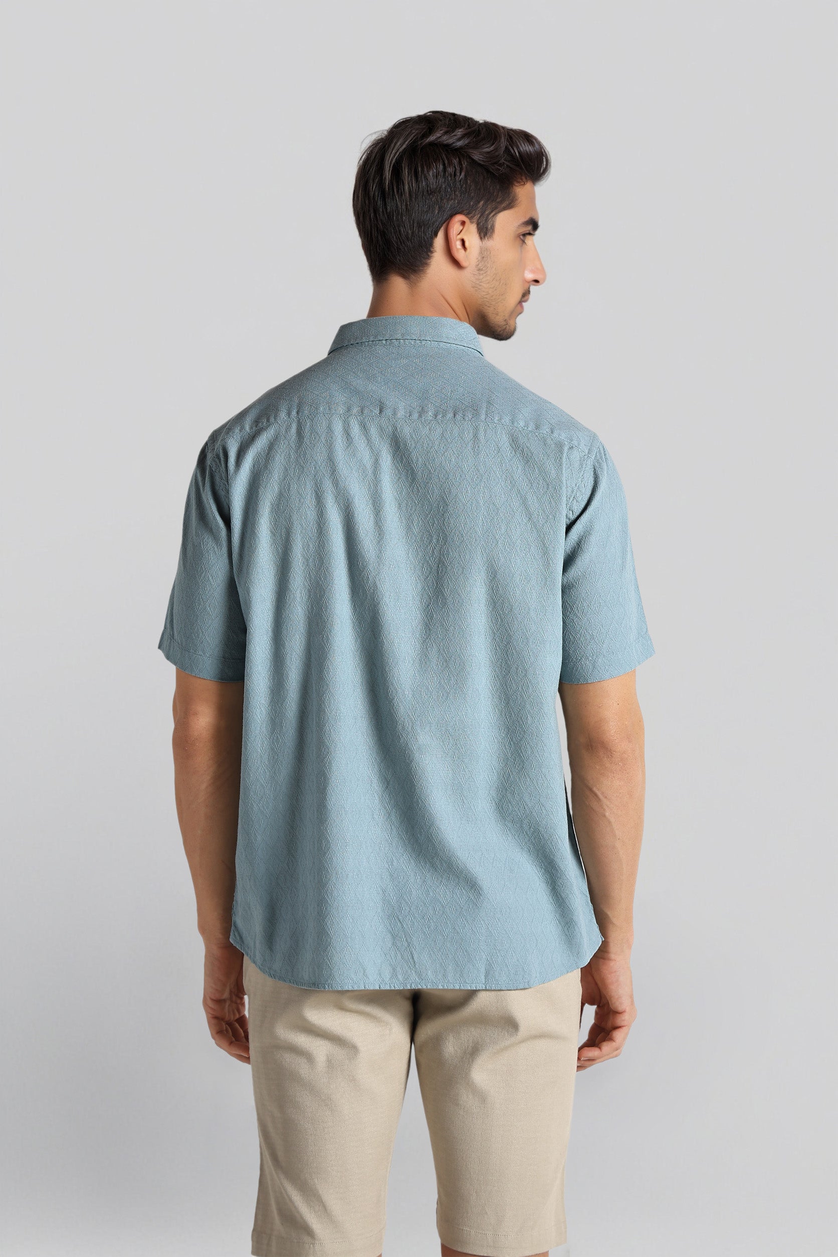 Man wearing a light blue short-sleeve shirt and beige pants on a plain background