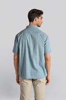 Man wearing a light blue short-sleeve shirt and beige pants on a plain background