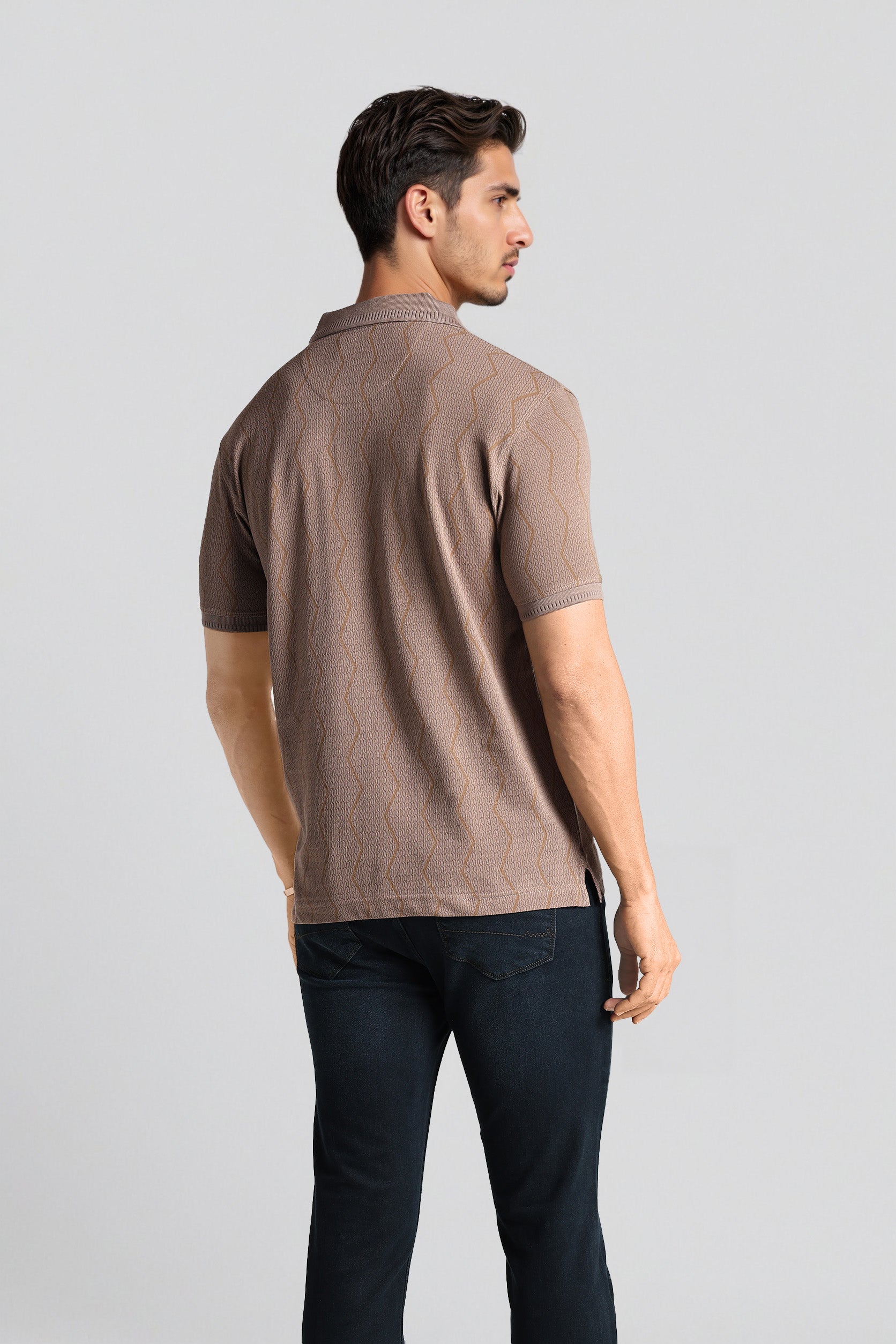 Man wearing a brown polo shirt and dark pants on a light gray background