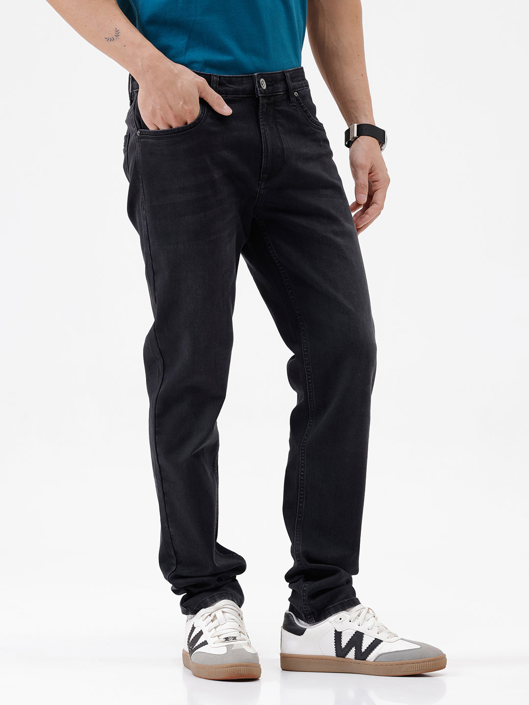 A person wearing slim-fit black jeans, a teal t-shirt, and white sneakers with gray accents, standing against a clean white studio background.