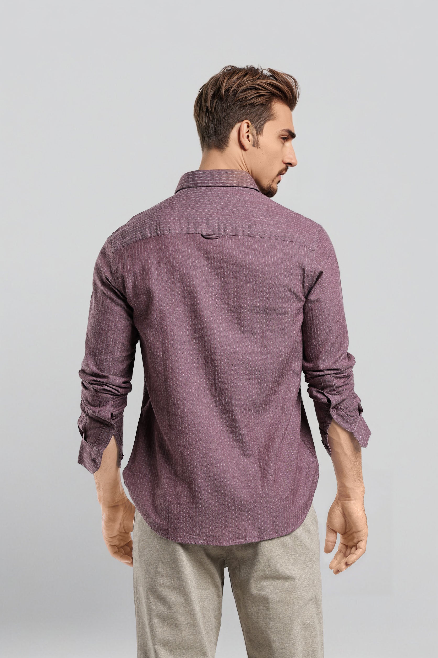 Man wearing a purple shirt and beige pants against a light gray background