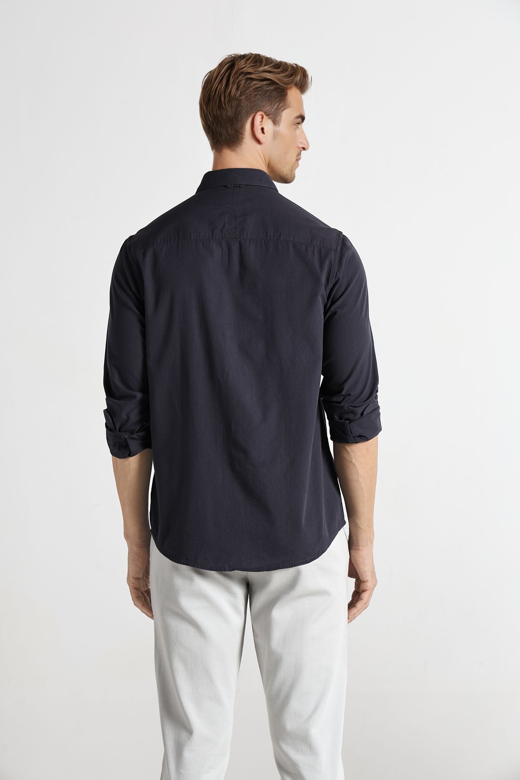 Man wearing a navy blue shirt and light gray pants on a white background