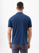 A man wearing a navy blue short-sleeve polo shirt with a subtle geometric pattern and a half-zip collar, paired with gray trousers, against a plain white background.