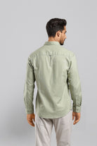 Man wearing a light green shirt and light gray pants on a plain background