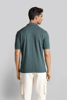 Man wearing a green textured polo shirt and white pants on a light gray background