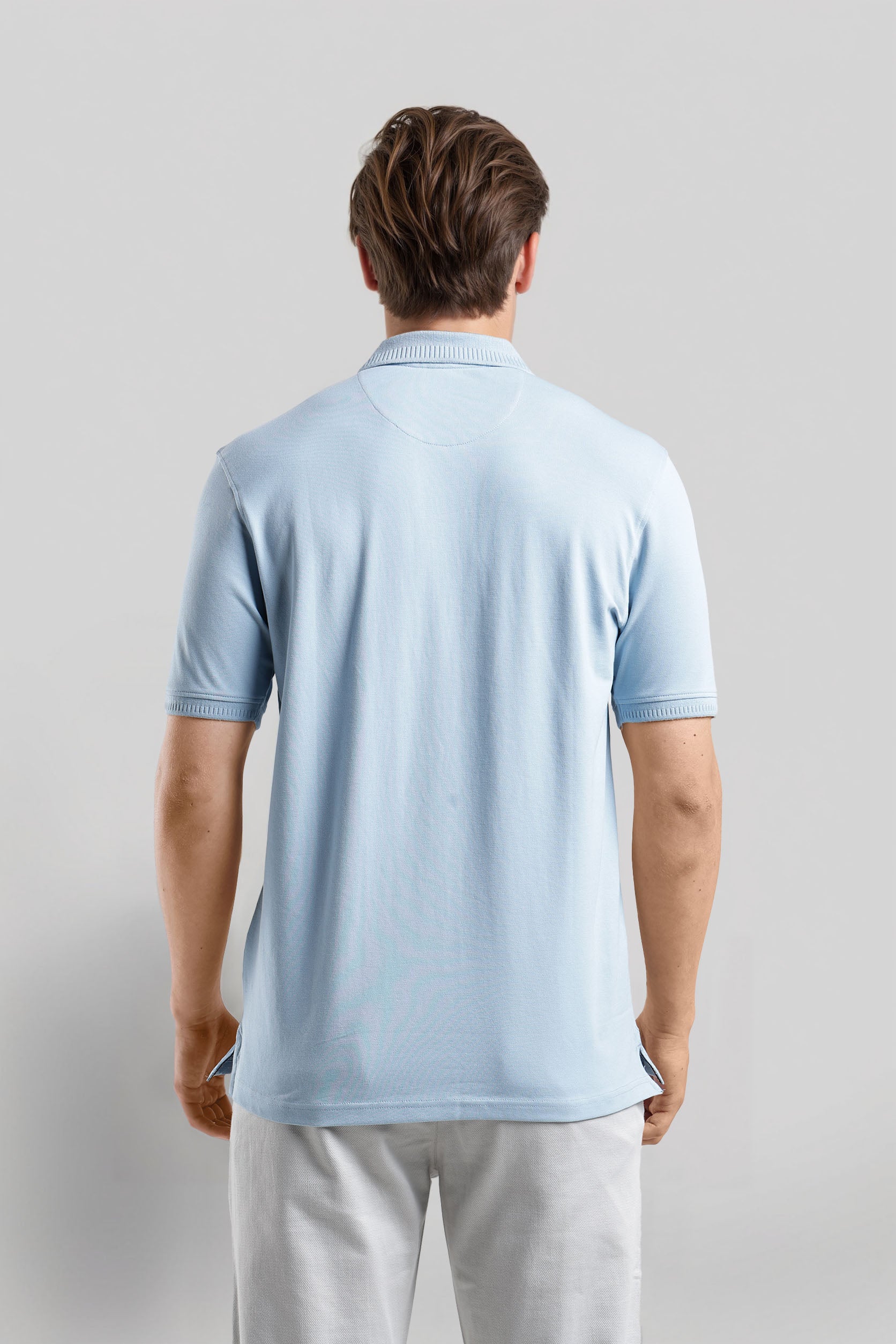 Man wearing a light blue polo shirt and light gray pants on a plain background