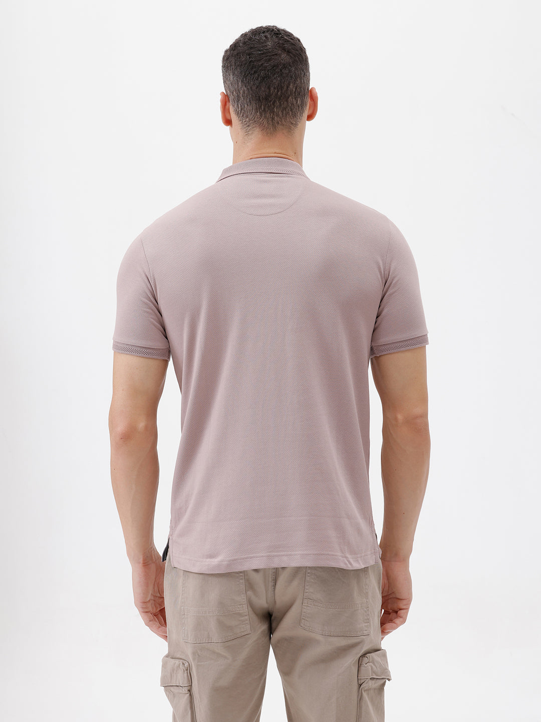 A man modeling a short-sleeve polo shirt in a dusty mauve-pink color, paired with khaki cargo pants and a baseball cap, against a plain light gray background.