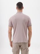 A man modeling a short-sleeve polo shirt in a dusty mauve-pink color, paired with khaki cargo pants and a baseball cap, against a plain light gray background.
