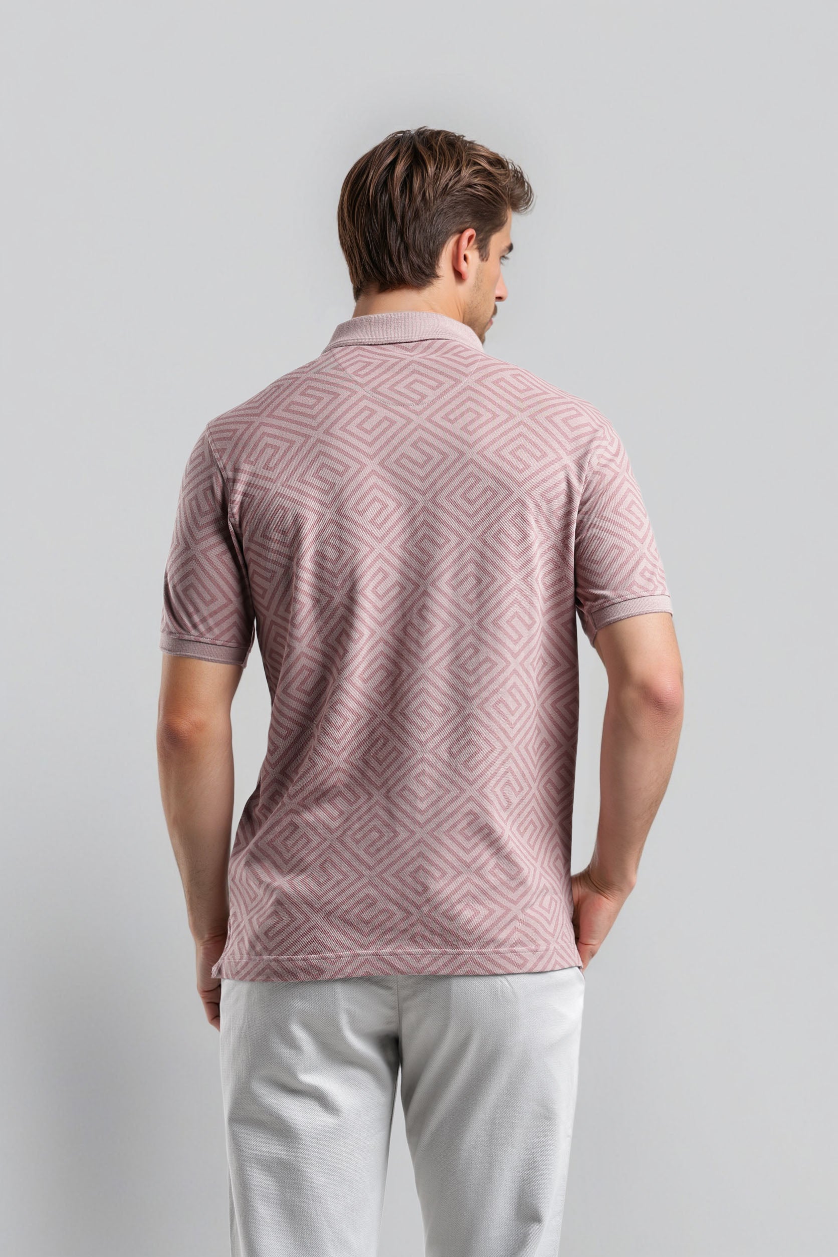 Man wearing a patterned pink polo shirt against a gray background