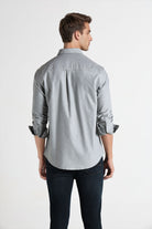 Man wearing a light gray button-up shirt and dark jeans on a white background