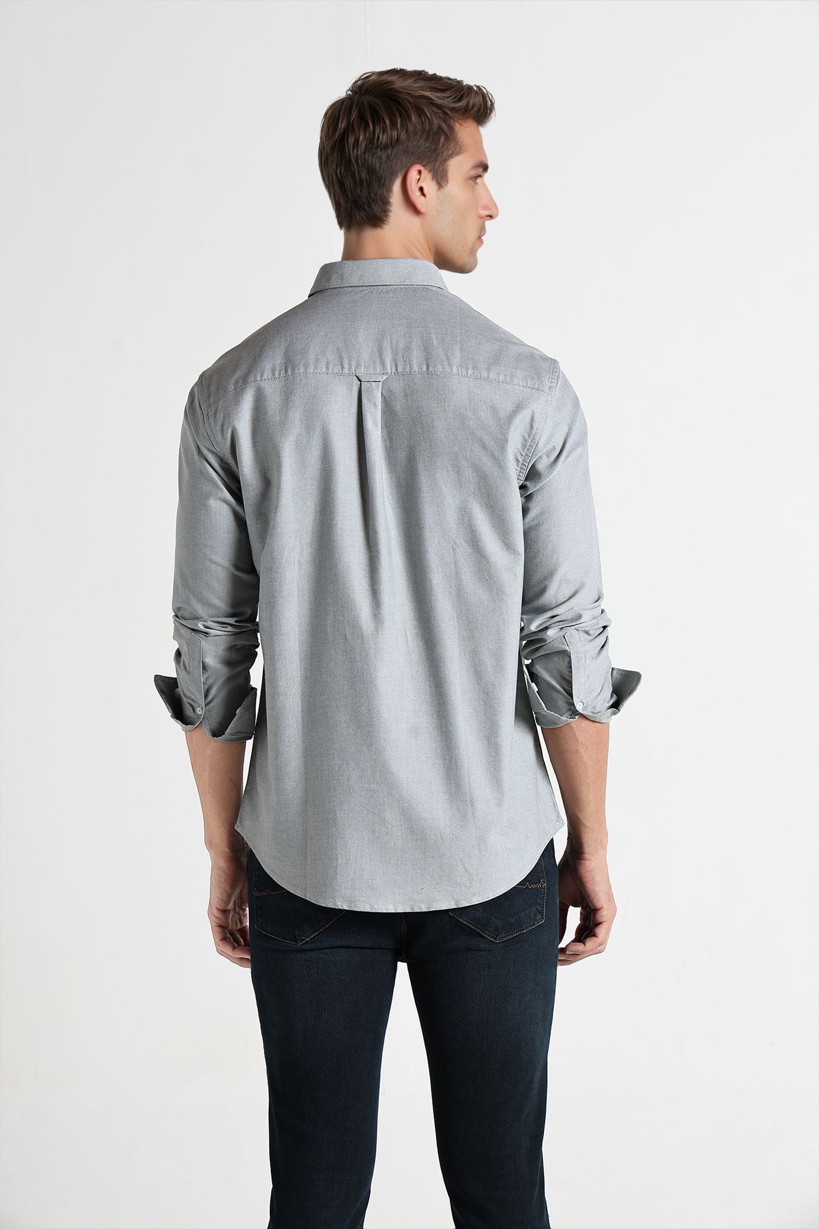 Man wearing a light gray button-up shirt and dark jeans on a white background