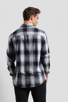 Man wearing a black and gray plaid shirt on a light gray background