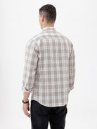 A man wearing a long-sleeve button-up plaid shirt in beige, white, and gray, paired with dark pants, standing against a plain white studio background.