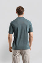 Man wearing a teal polo shirt and light gray pants on a white background