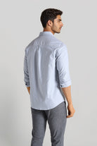 Man wearing a light blue shirt and gray pants on a plain background