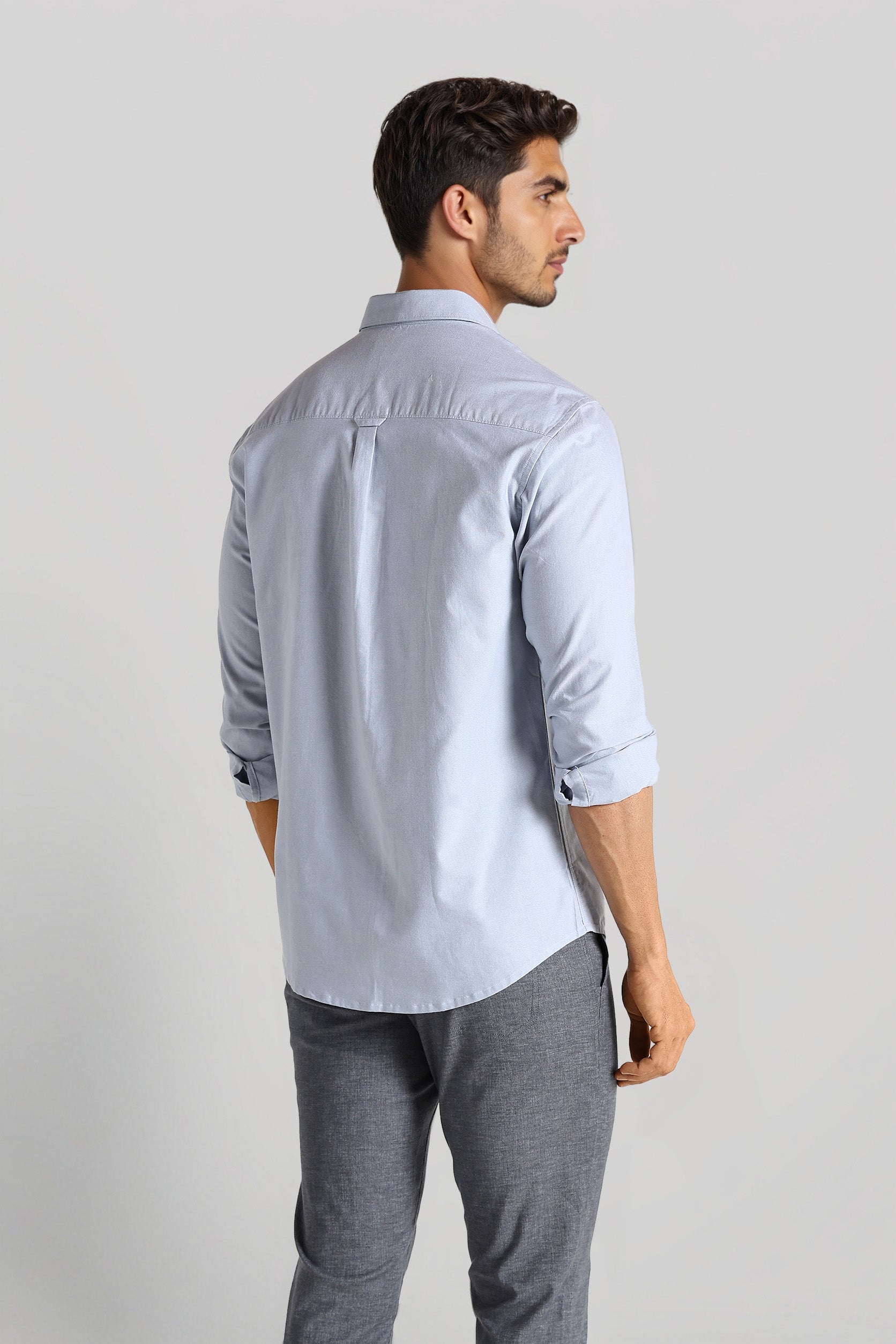 Man wearing a light blue shirt and gray pants on a plain background