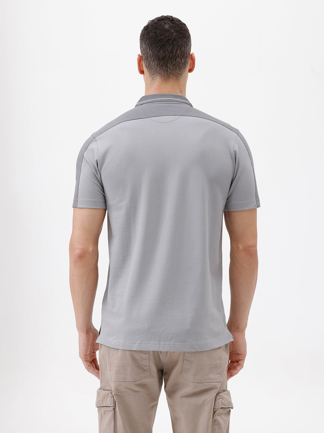 A man wearing a light gray short-sleeve polo shirt with darker gray shoulder panels and a small crest logo on the left chest, paired with khaki cargo pants, against a plain light gray studio background.