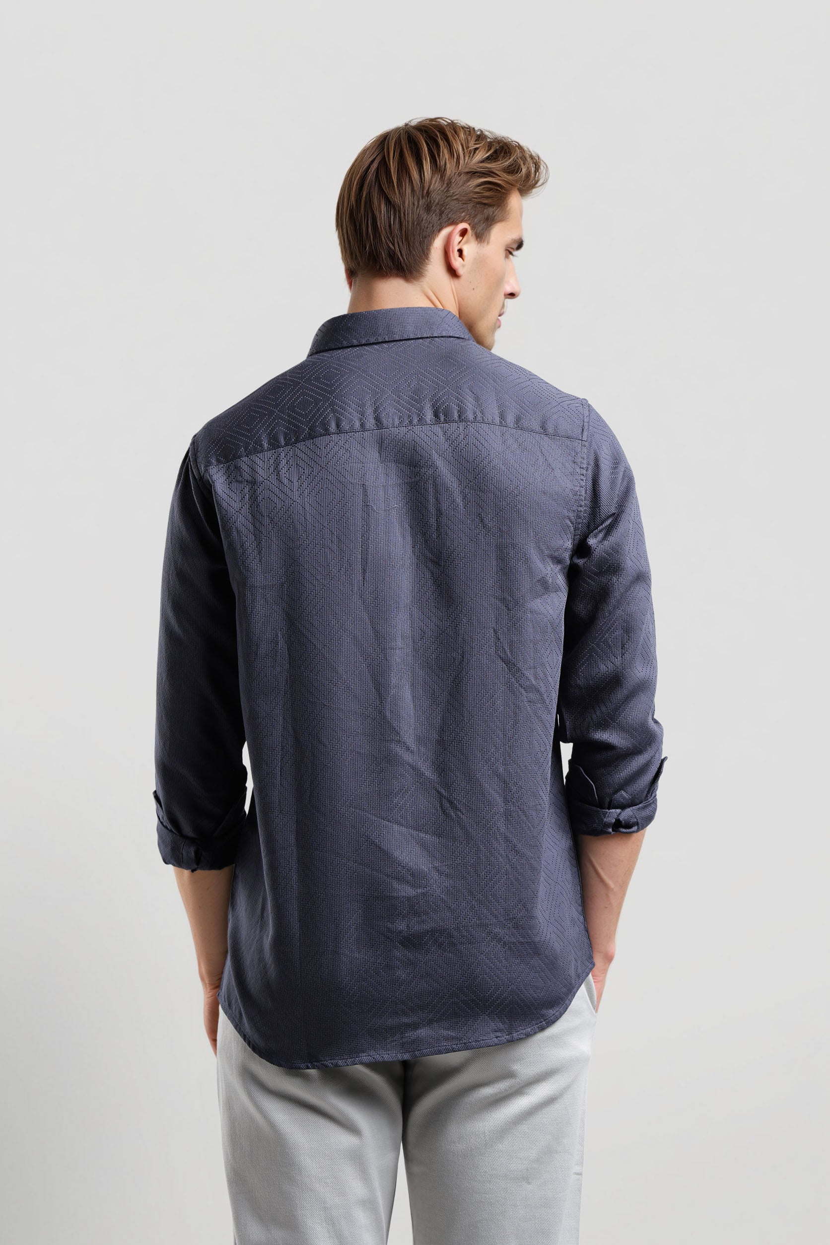 Man wearing a dark blue button-up shirt and light gray pants on a white background