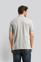 Man wearing a light gray polo shirt and blue jeans on a plain background