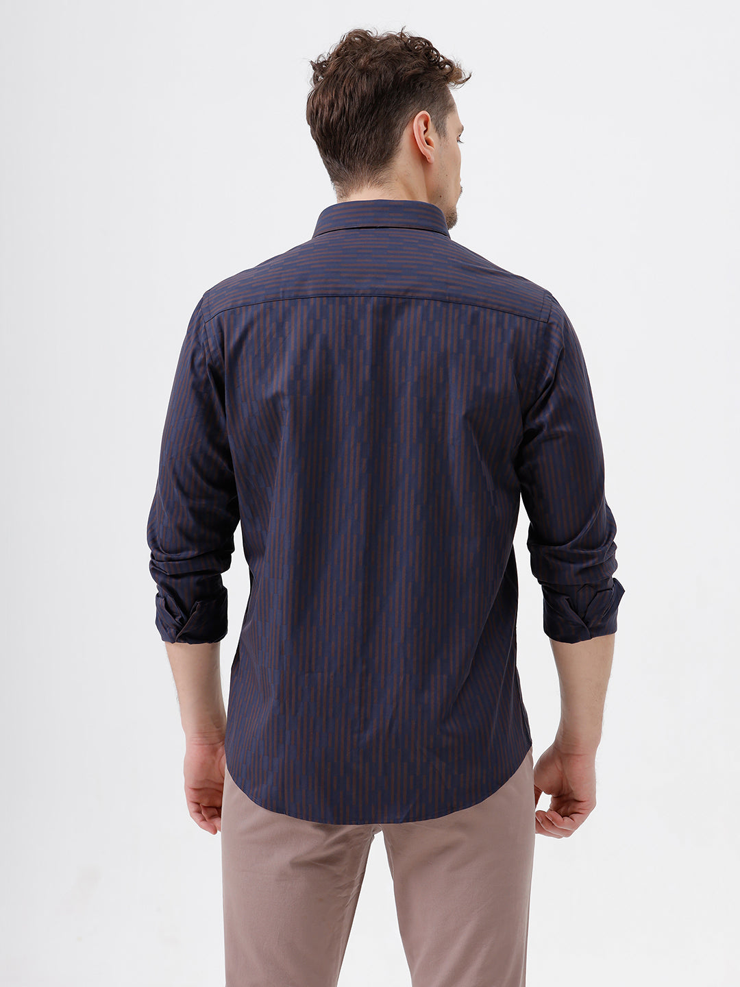 A man wearing a dark navy blue button-down shirt with thin vertical red stripes and light brown trousers, standing against a plain white studio background.