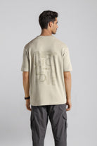 Man wearing a beige t-shirt with text on the back against a plain background