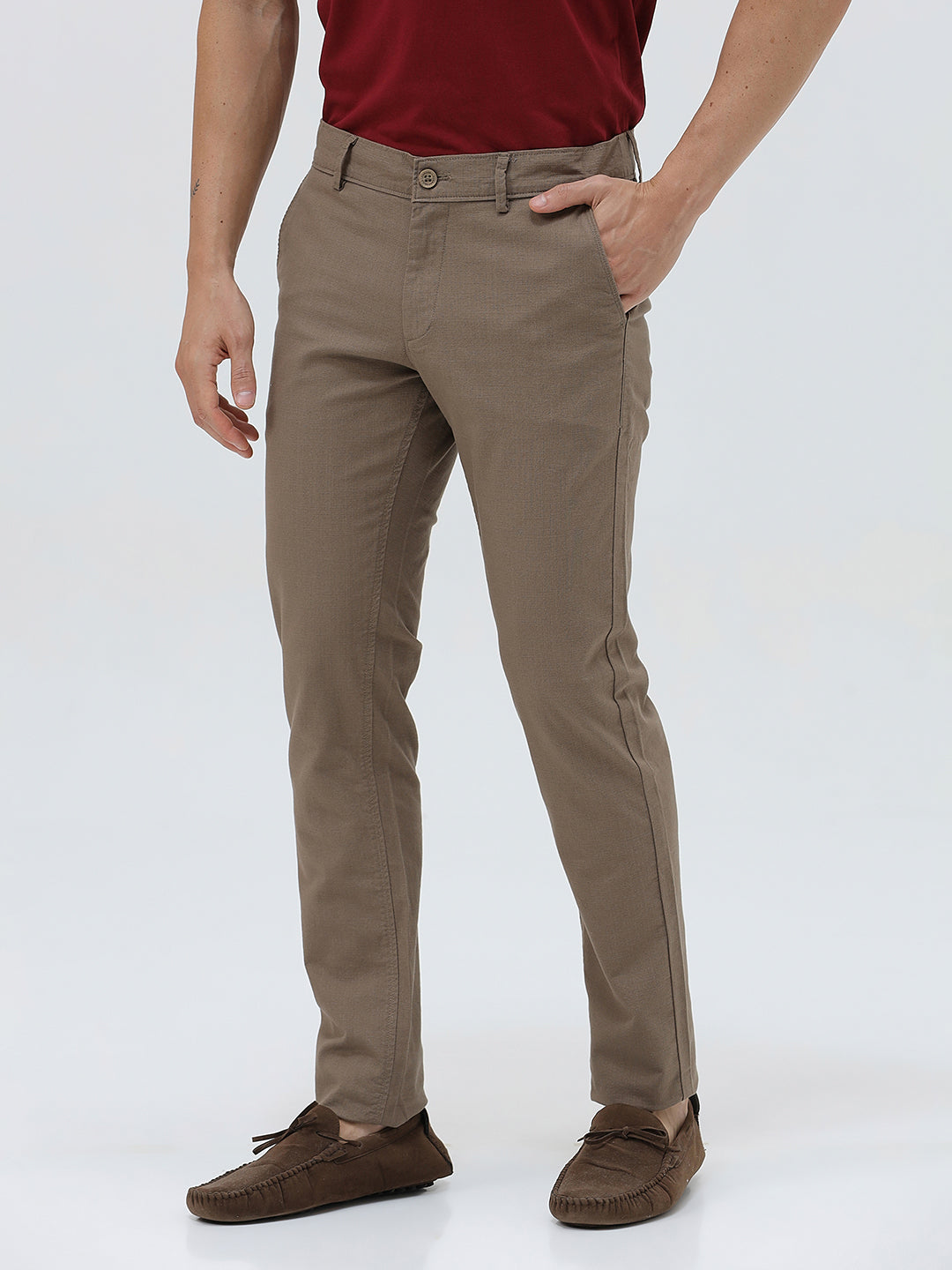 A person wearing slim-fit brown trousers, paired with a dark red shirt and brown suede moccasin shoes, shown from the waist down against a plain white studio background.