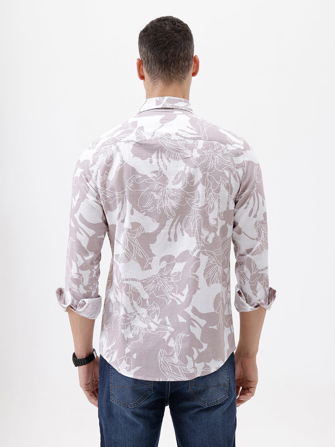 A man wearing a long-sleeve button-up shirt with a light gray and white abstract floral pattern, paired with dark blue jeans, standing against a plain white background.