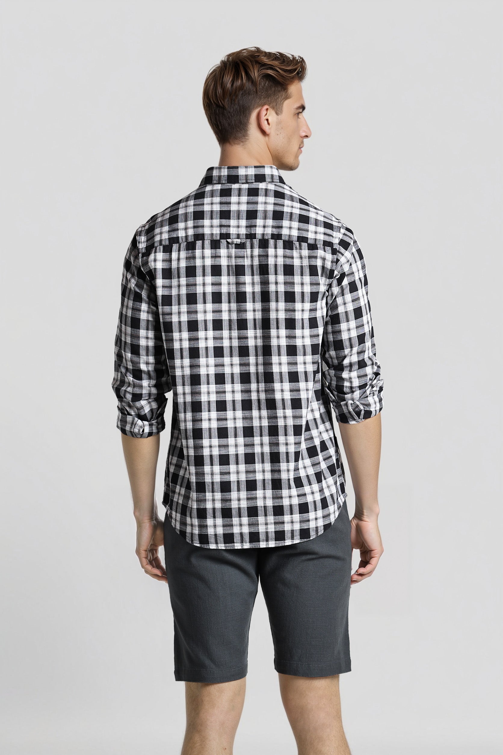 Man wearing a black and white checkered shirt and gray shorts on a light gray background