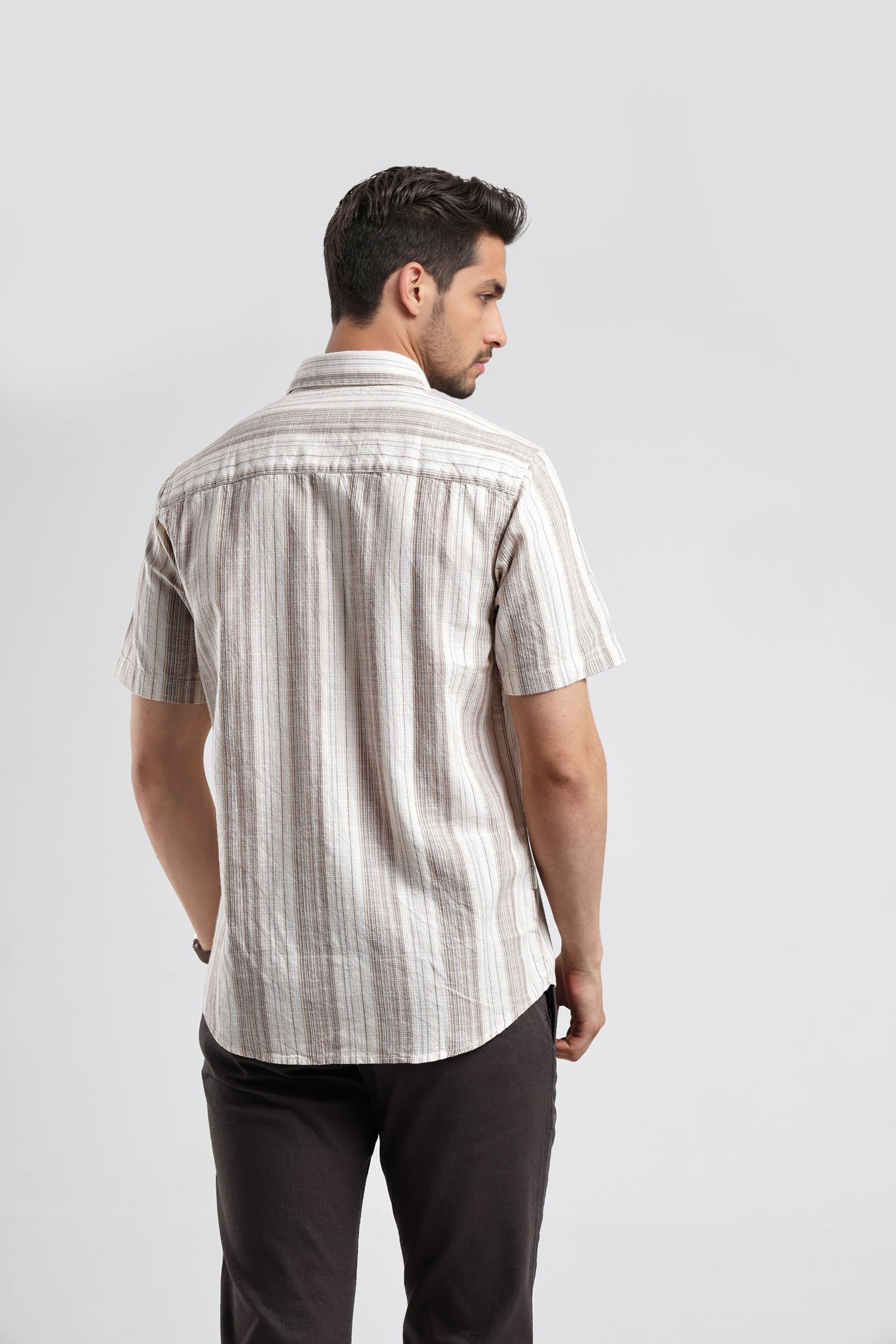 Man wearing a striped shirt and dark pants on a light gray background