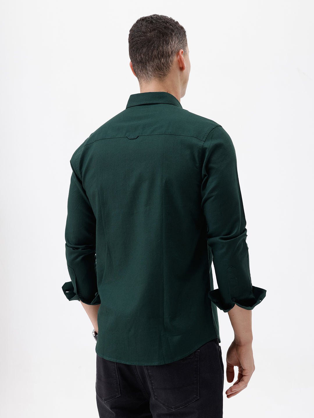A man wearing a dark forest green long-sleeve button-down shirt with a chest pocket, paired with dark jeans, standing against a plain white studio background.