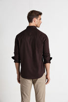 Man wearing a brown shirt and beige pants on a white background