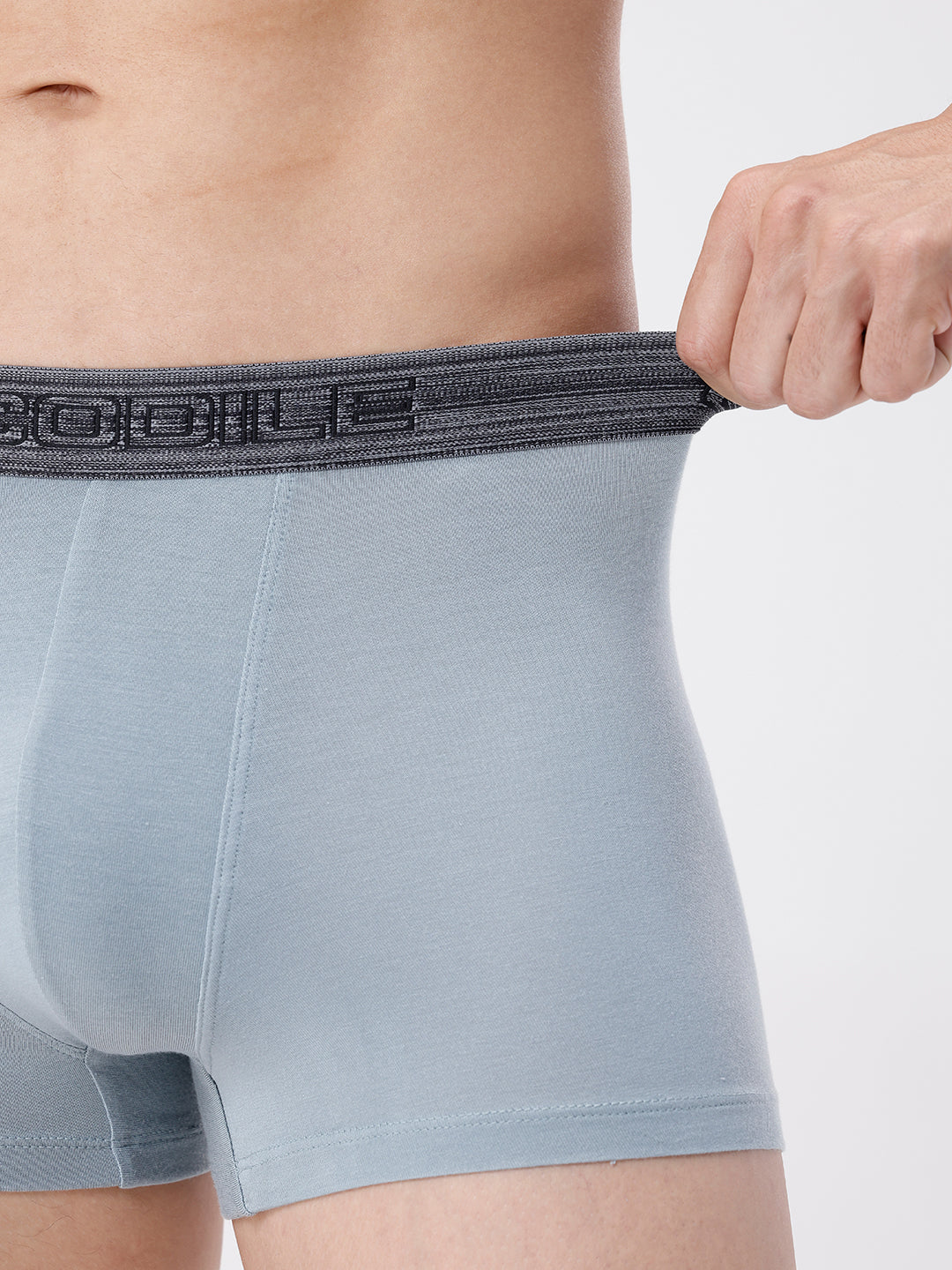 Light blue boxer briefs with a dark waistband being adjusted on a plain background