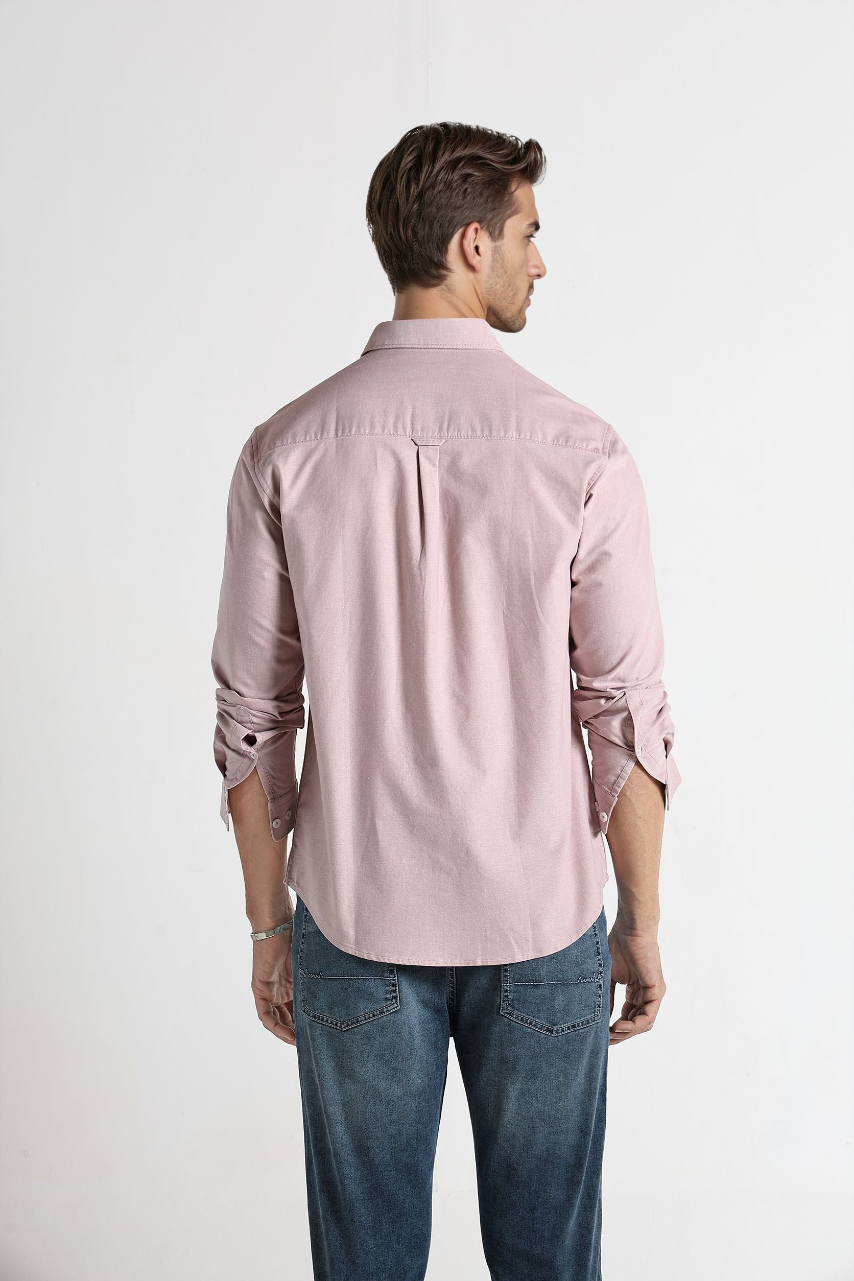 Man wearing a light pink shirt and blue jeans on a white background