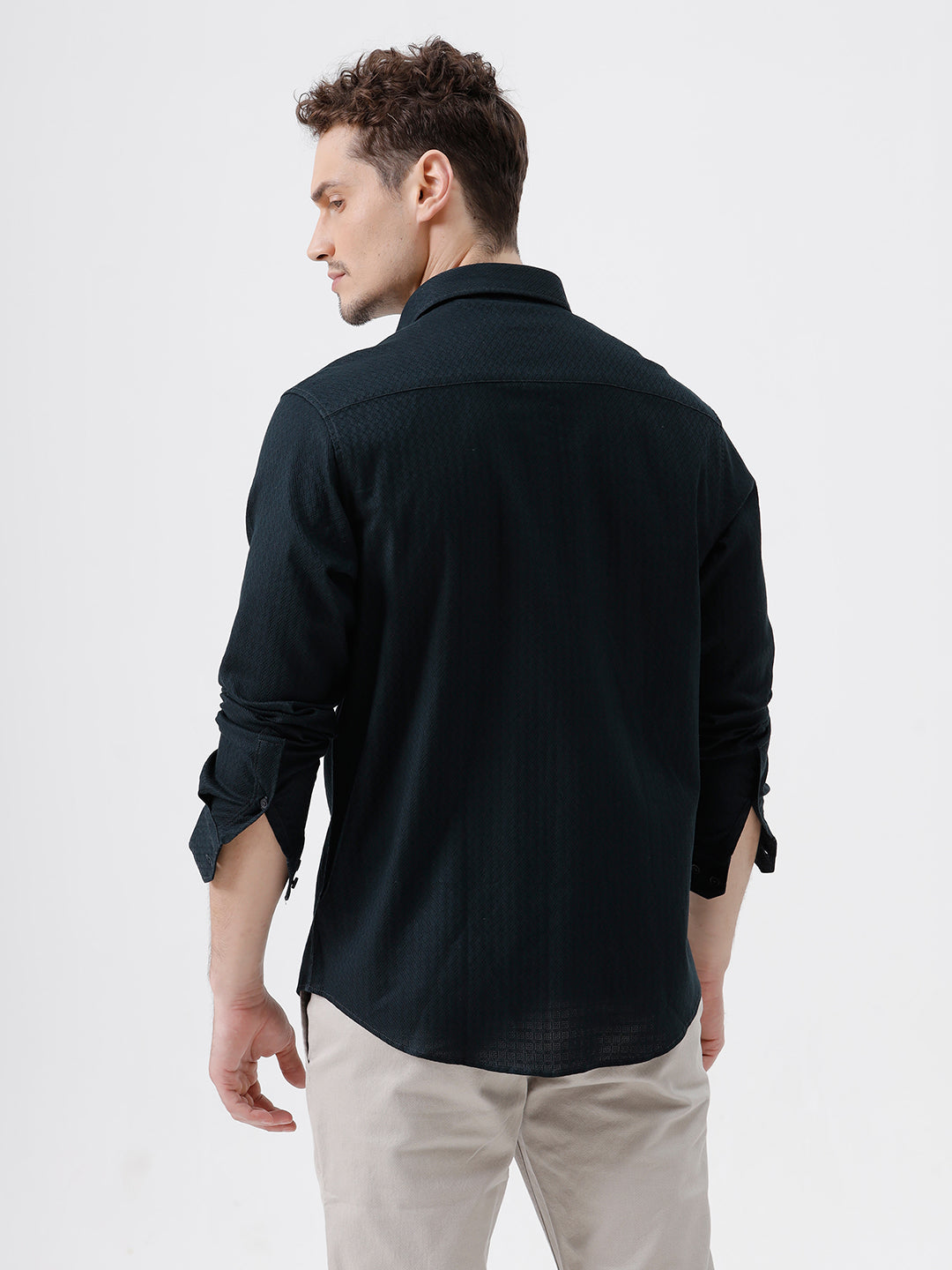 A man wearing a dark navy long-sleeve button-up shirt with a subtle textured pattern and light beige trousers, standing against a plain light gray background.