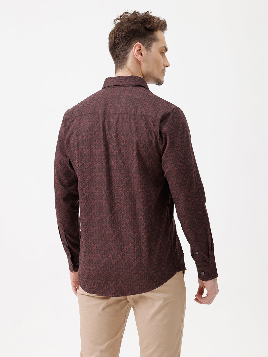A man wearing a dark burgundy long-sleeve button-up shirt with a subtle geometric pattern, paired with beige trousers, standing against a plain white studio background.