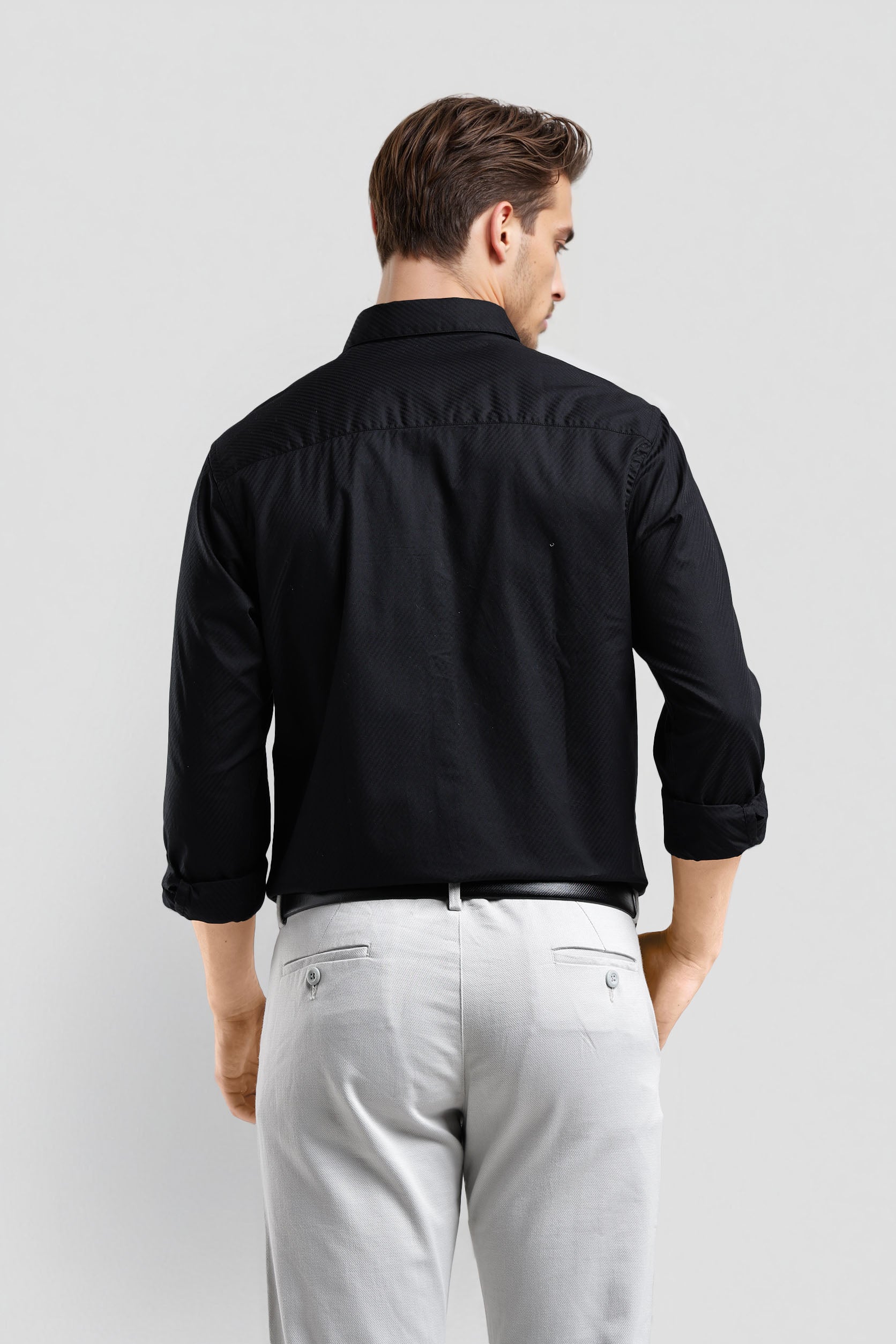 Man wearing a black shirt and gray pants on a light gray background