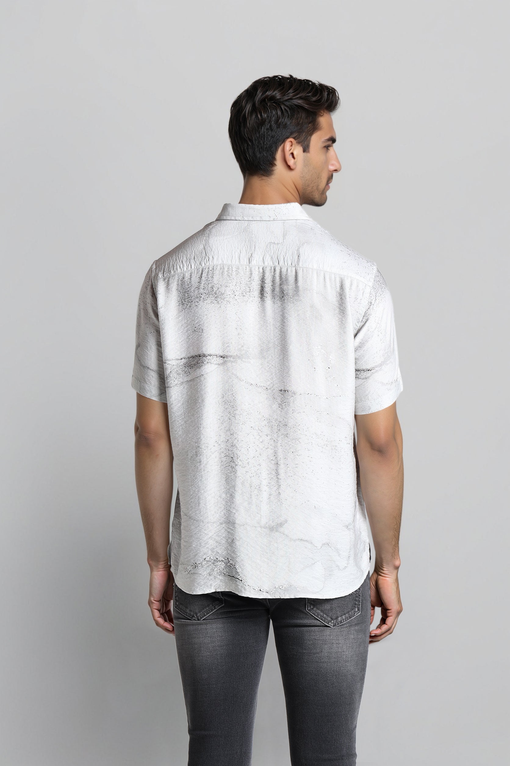 Man wearing a white short-sleeve shirt and dark jeans on a light gray background