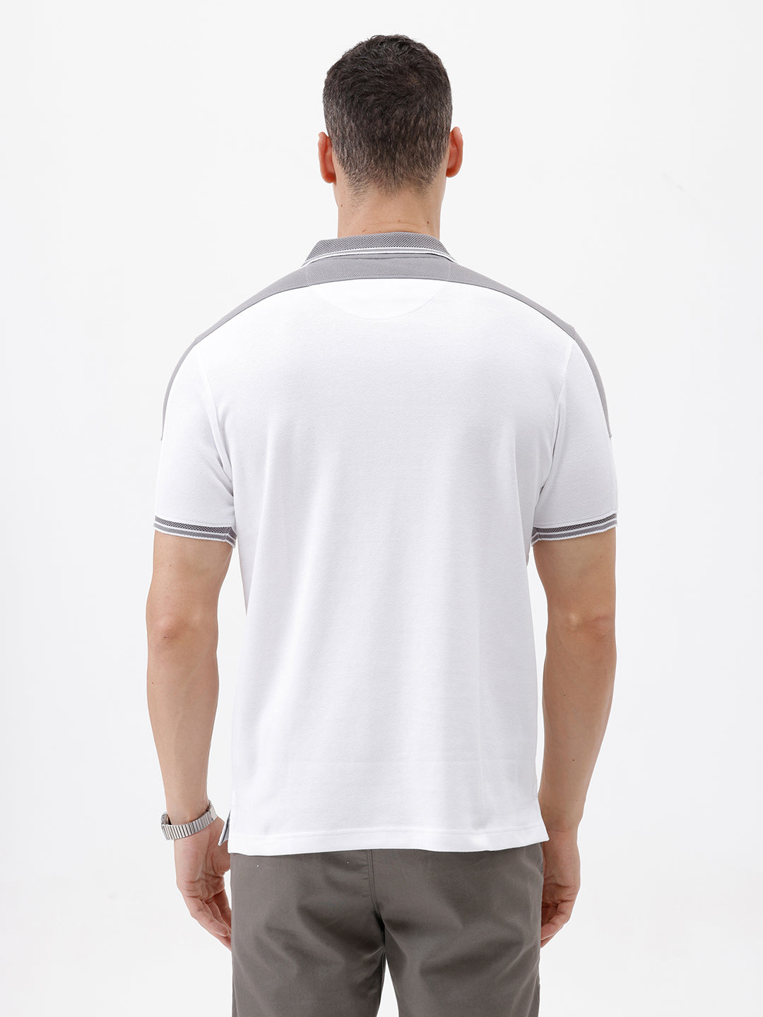 A man modeling a white short-sleeve polo shirt with gray shoulder panels and gray striped trim on the sleeves, paired with gray trousers and black sunglasses, against a plain white background.