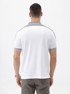 A man modeling a white short-sleeve polo shirt with gray shoulder panels and gray striped trim on the sleeves, paired with gray trousers and black sunglasses, against a plain white background.