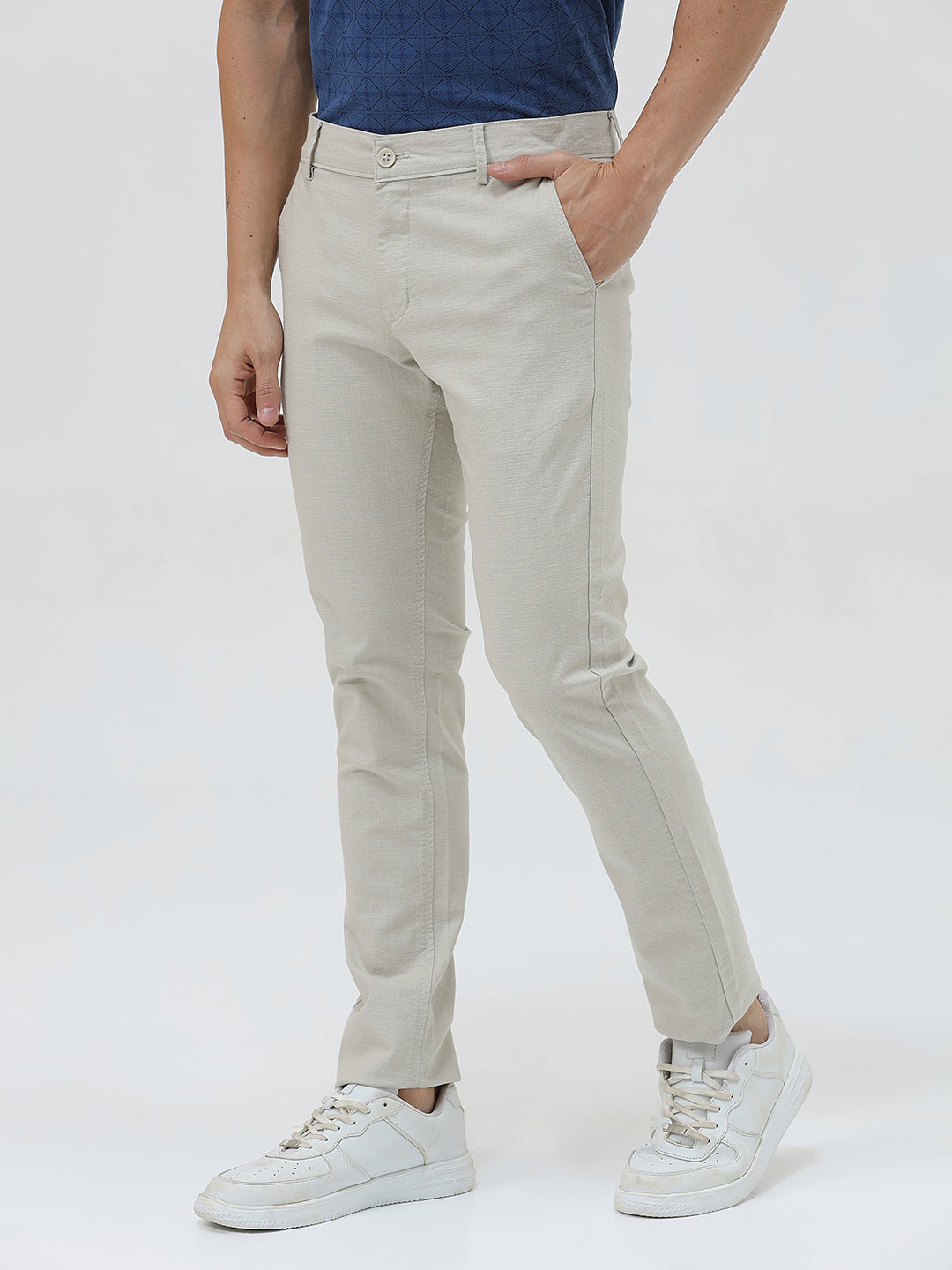 A person wearing light beige slim-fit chino pants, a navy blue t-shirt, and white sneakers, standing against a plain white studio background.
