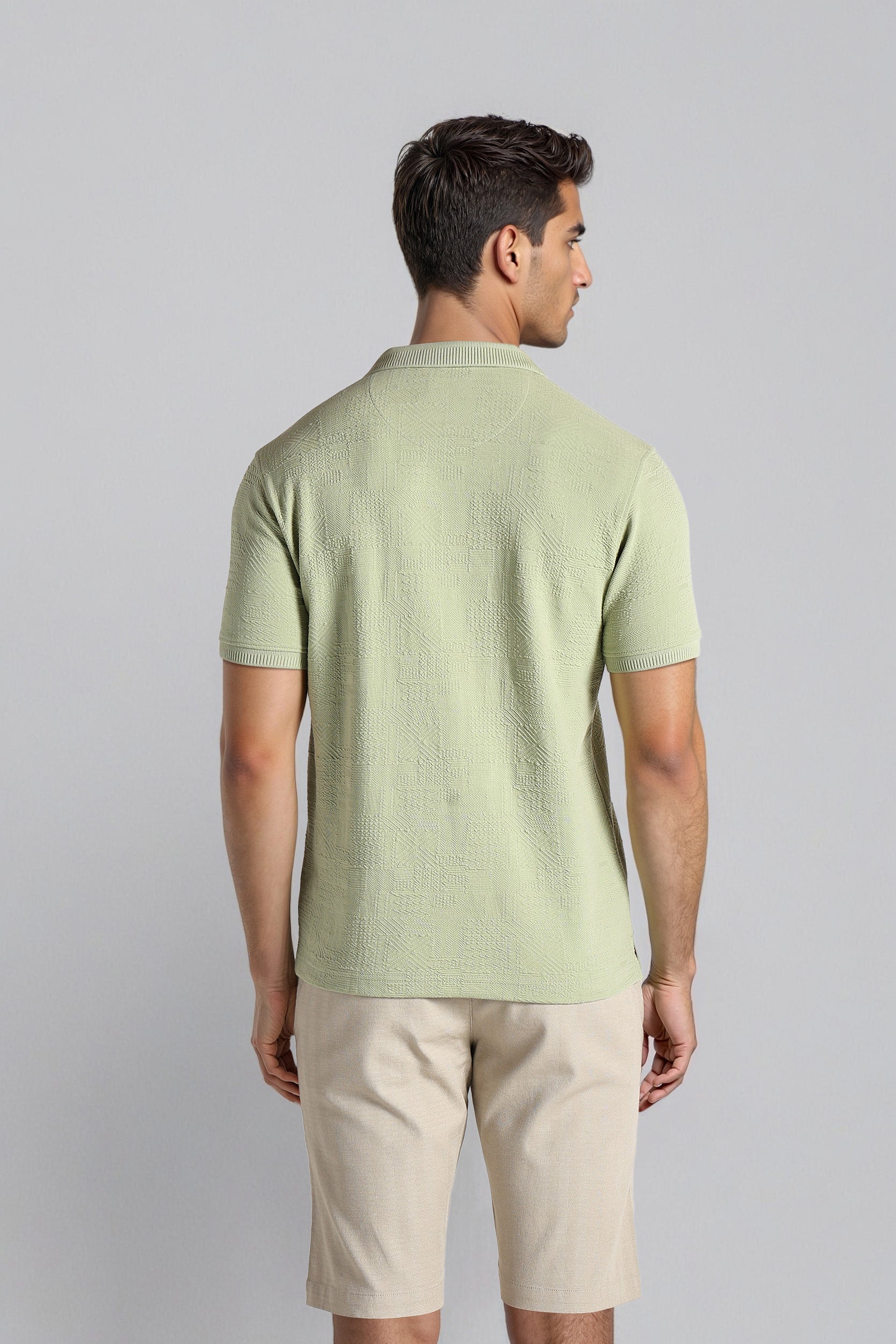 Man wearing a light green textured t-shirt and beige shorts on a gray background