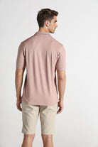 Man wearing a pink polo shirt and beige shorts on a white background