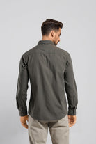 Man wearing a dark green shirt and beige pants on a light gray background