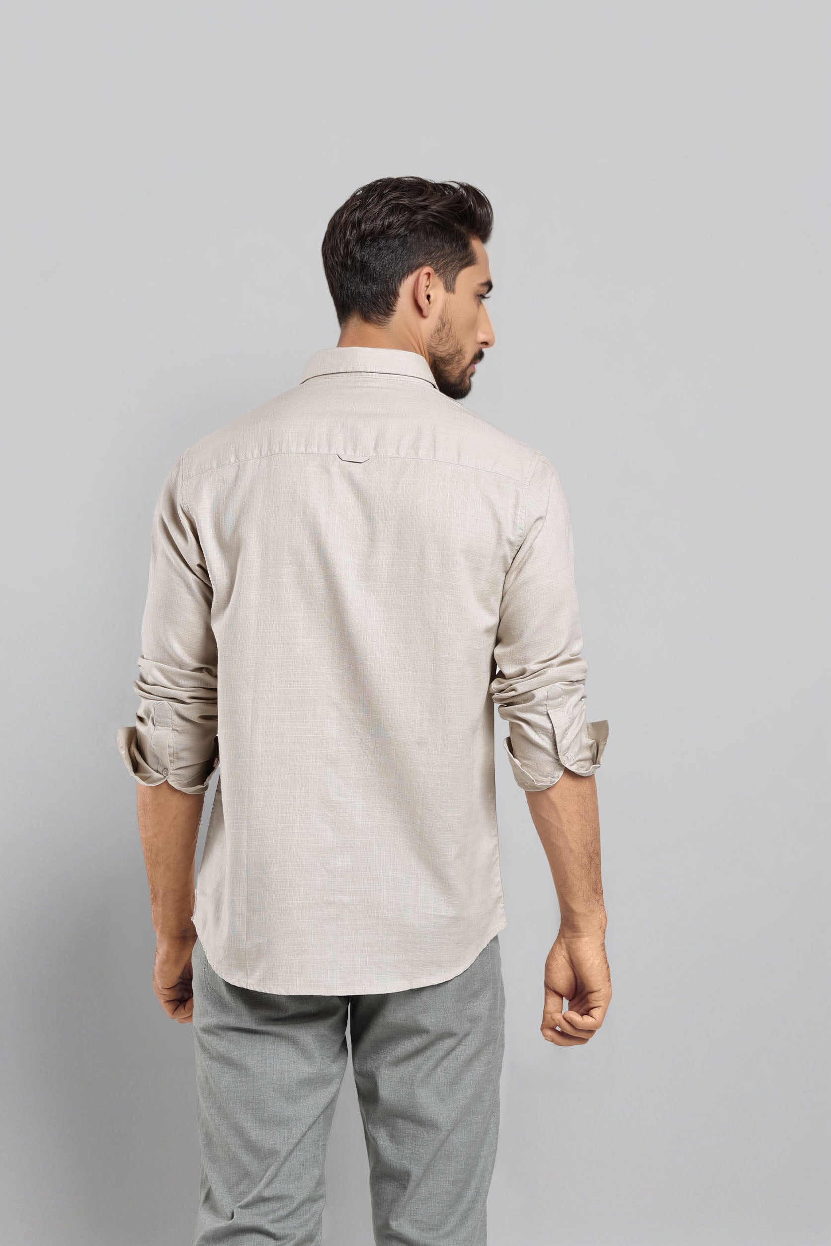 Man wearing a beige shirt and gray pants against a light gray background