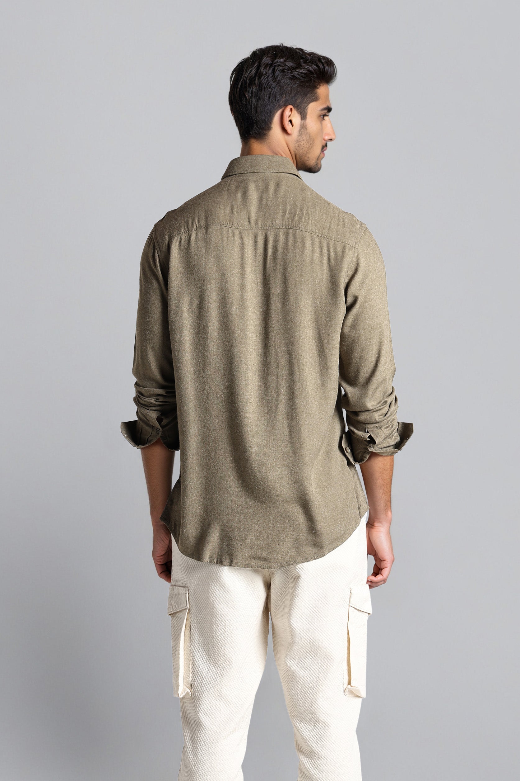 Man wearing a brown shirt and white pants against a gray background