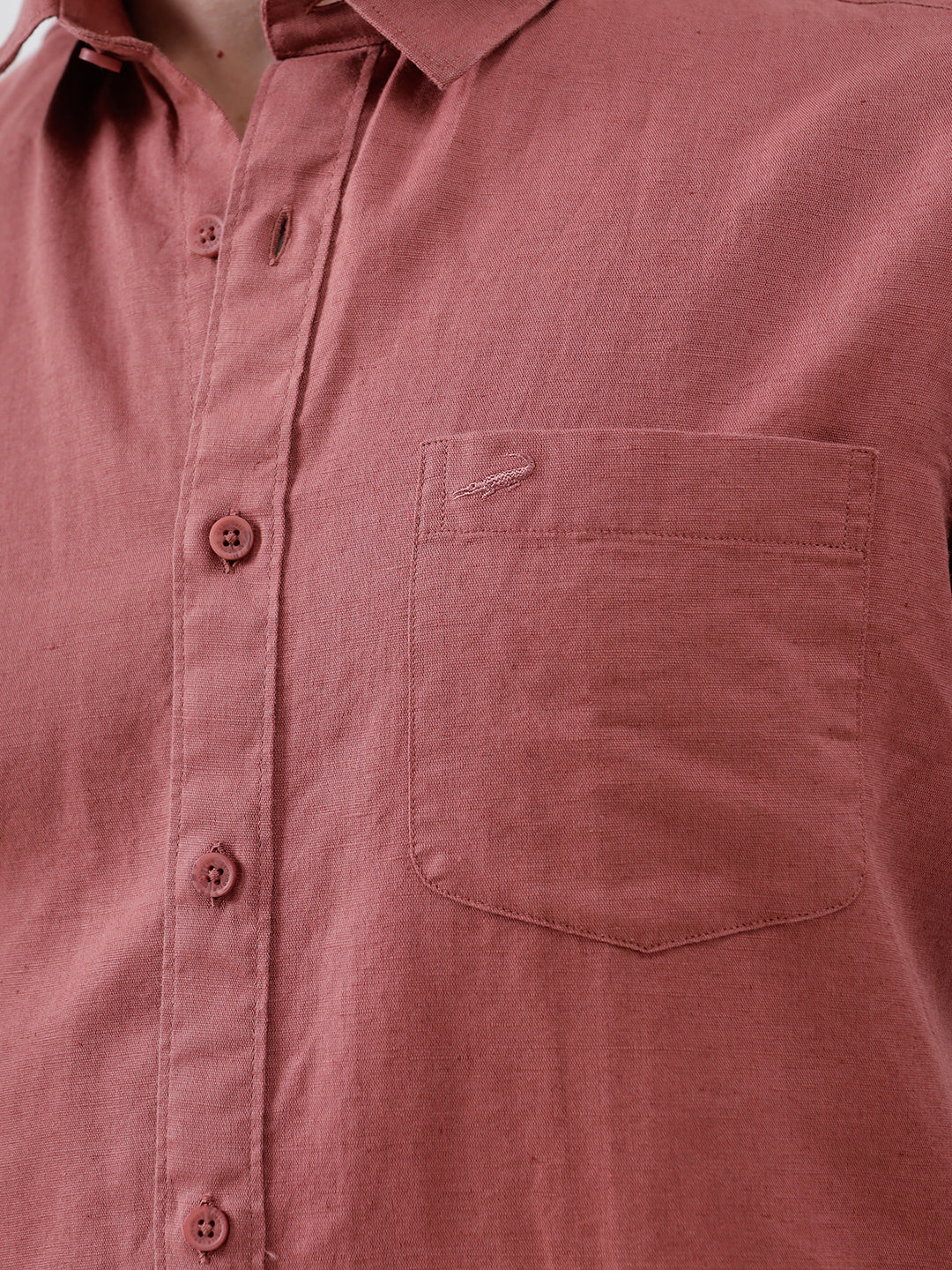 A man wearing a short-sleeve button-up shirt in a dusty rose color, paired with beige trousers, standing against a light gray studio background.