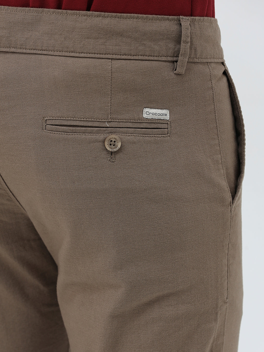 A person wearing slim-fit brown trousers, paired with a dark red shirt and brown suede moccasin shoes, shown from the waist down against a plain white studio background.