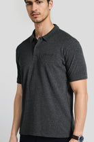 Man wearing a dark gray polo shirt with a brand logo on a light gray background